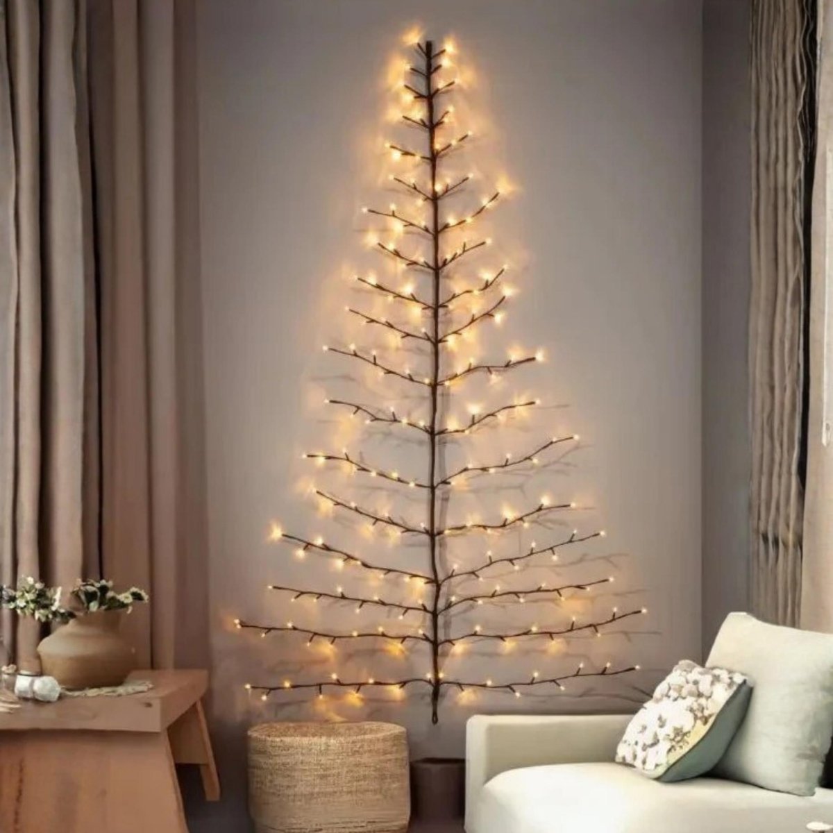 A slim, minimalist tree-shaped light fixture with warm white LED lights mounted on a gray wall in a cozy living room setting next to a white sofa and curtains.