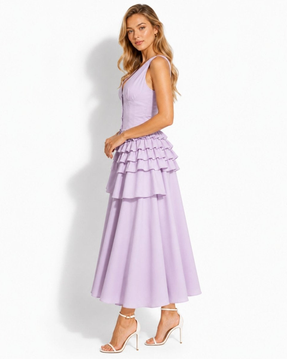 A woman modeling a sleeveless lavender maxi dress with a structured bodice and a tiered ruffle skirt, paired with clear high-heeled sandals, against a plain white studio background.