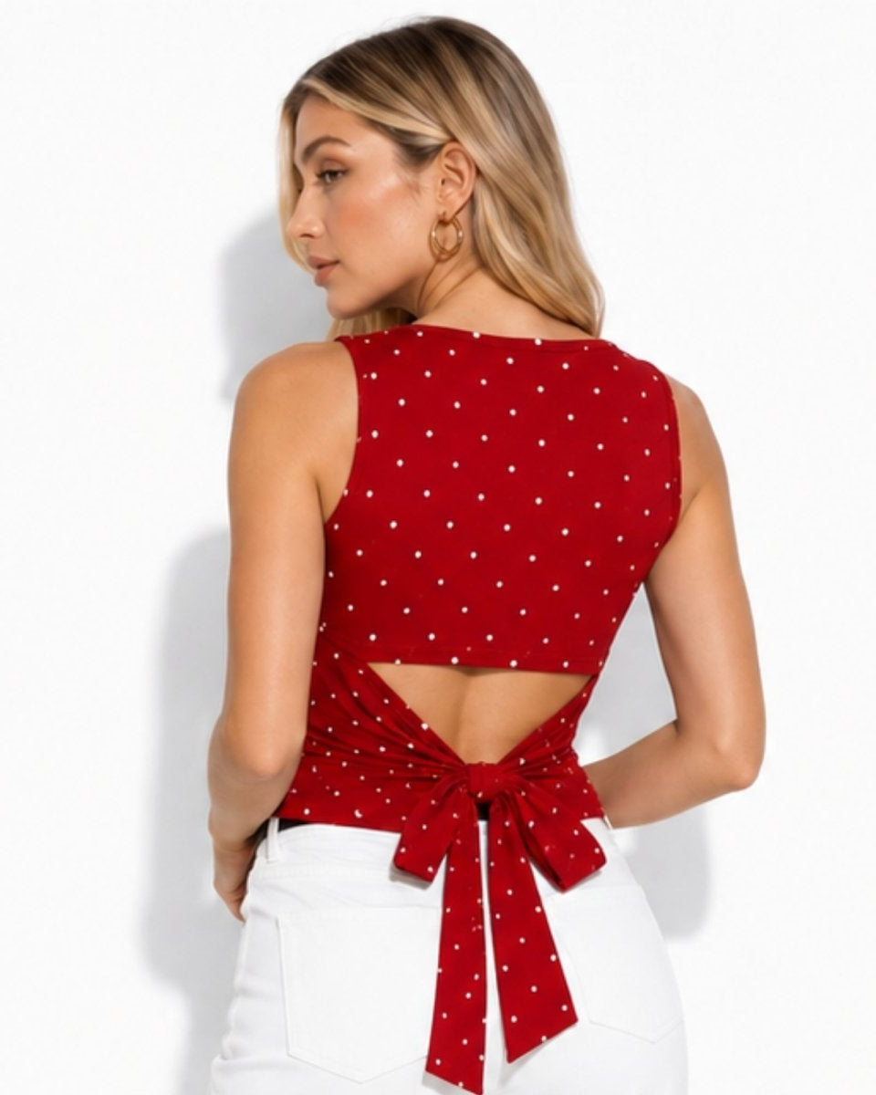 A woman shown from the back wearing a red sleeveless crop top with a white polka dot pattern and a tie detail at the waist, paired with white pants against a light gray studio background.