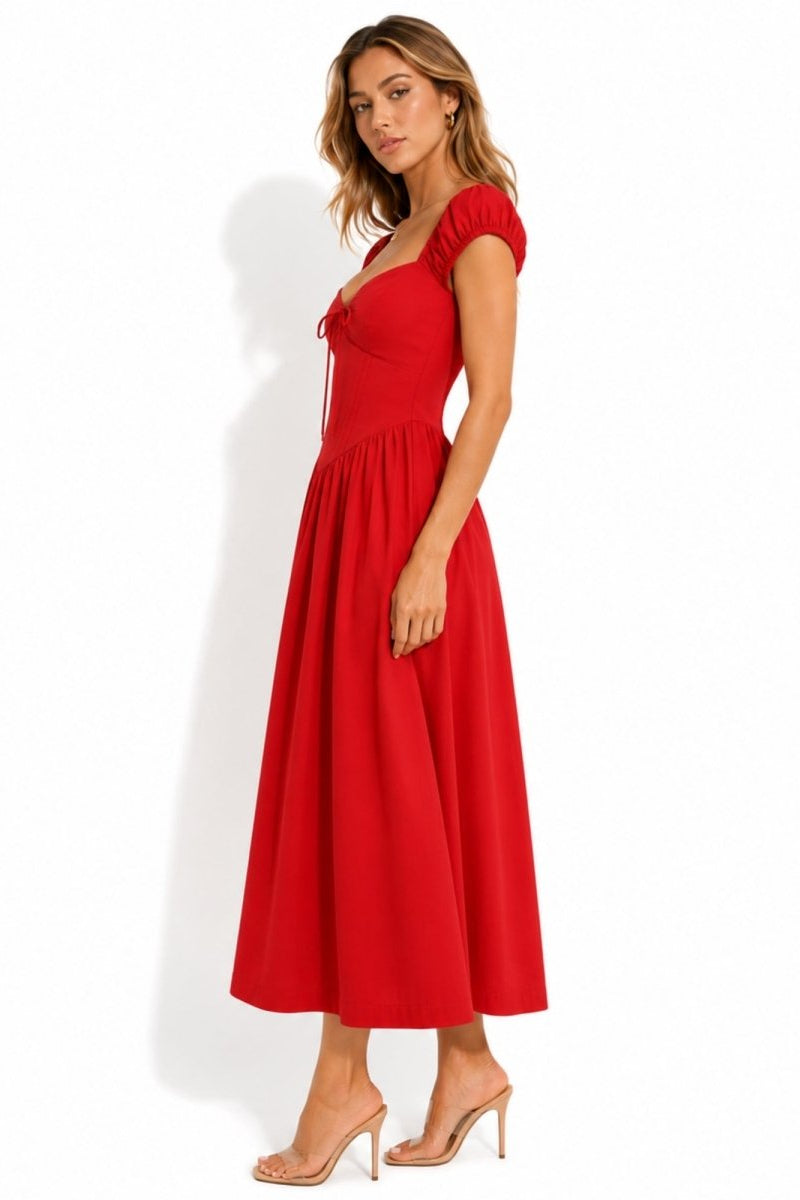 A woman modeling a bright red midi dress with short puff sleeves, a sweetheart neckline, and a flared skirt, paired with nude high-heeled sandals against a white studio background.