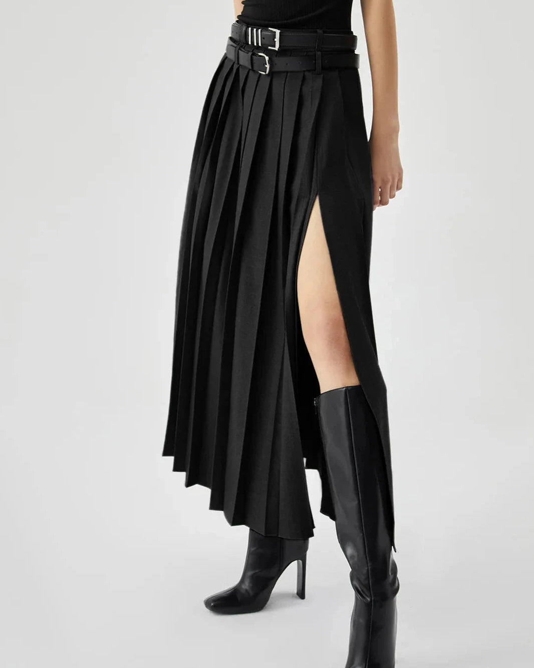 Person wearing a black pleated skirt with a high slit and black boots on a white background