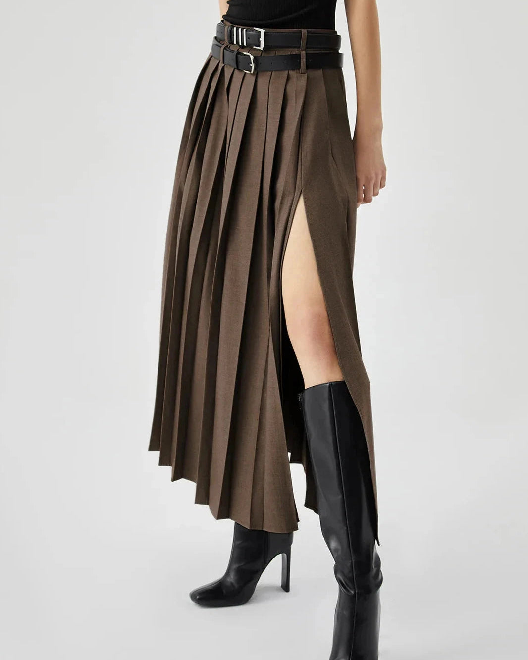 Person wearing a brown pleated skirt with a high slit and black boots on a white background