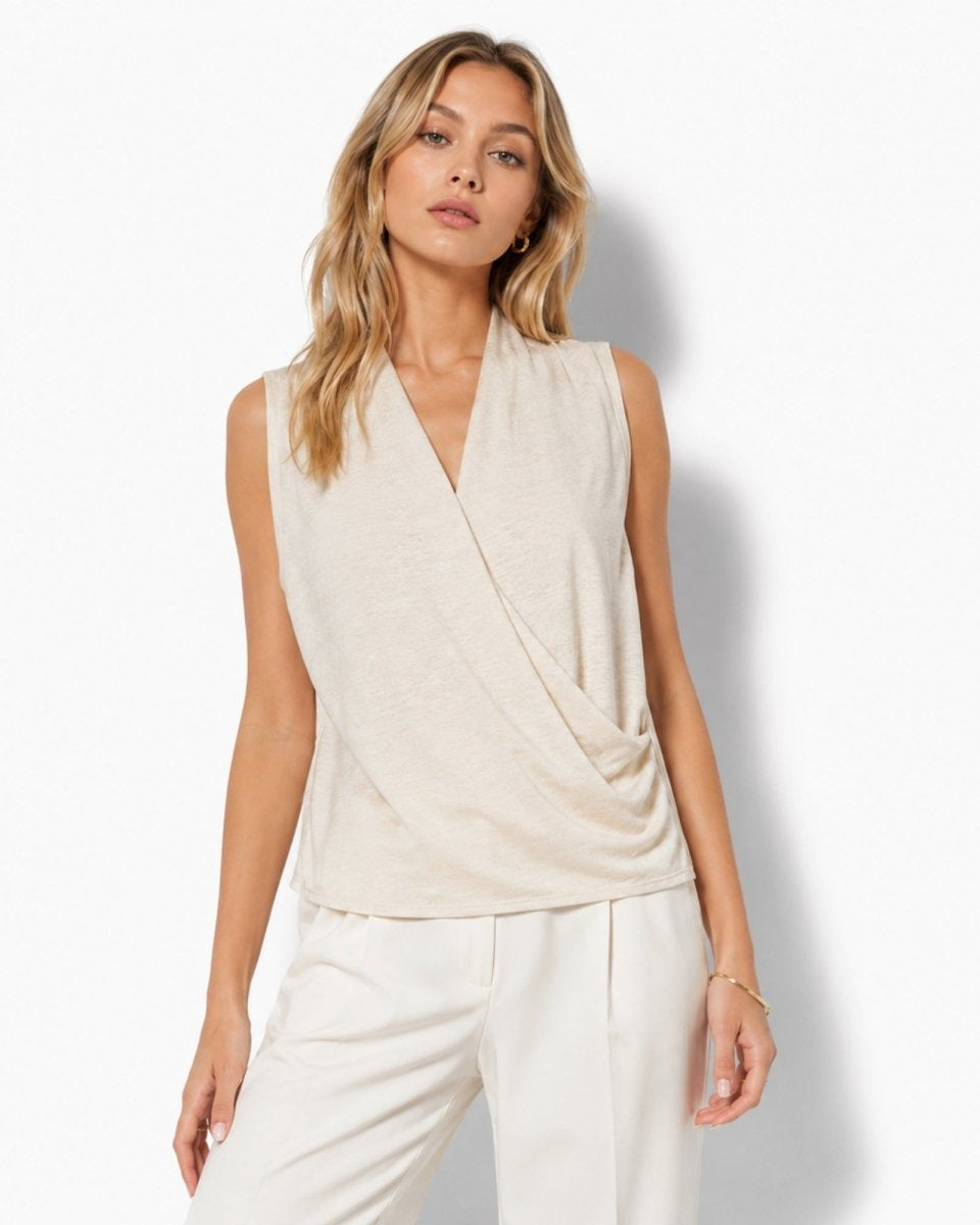Woman wearing a sophisticated beige sleeveless draped wrap blouse with a v-neckline by Fenlo Form, styled with tailored cream trousers.