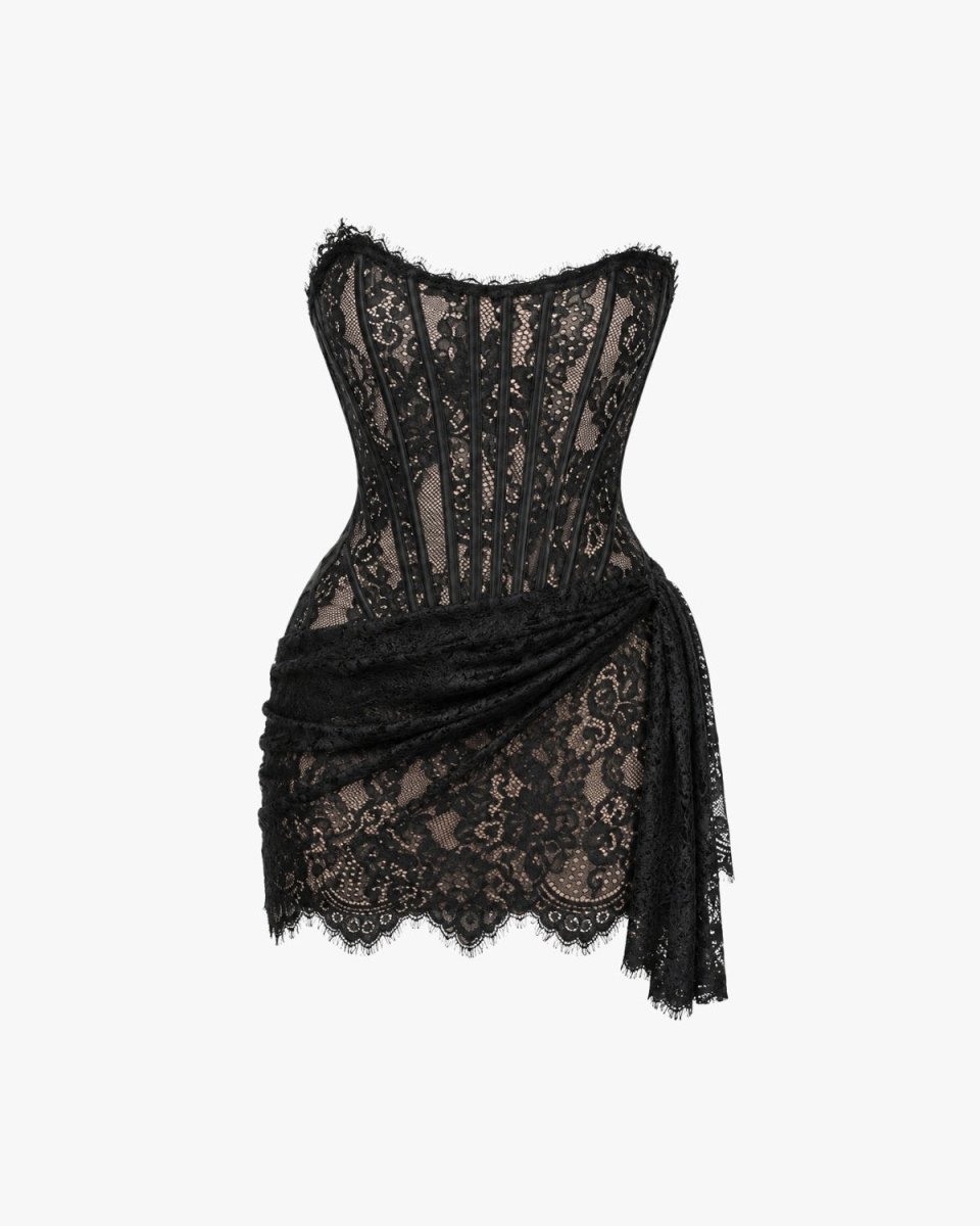 A black lace corset mini dress with a sheer corset-style bodice, scalloped lace trim, and a draped wrap skirt, shown against a plain light gray background.