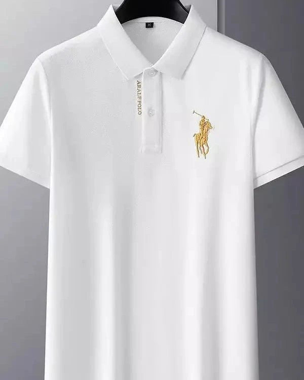White polo shirt with a gold logo on a hanger against a gray background