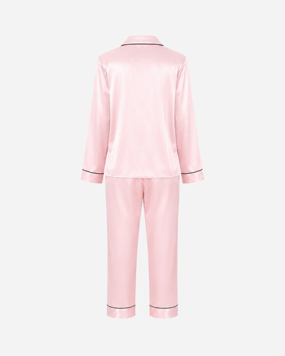 A light pink satin pajama set shown from the back, featuring a long-sleeve top and matching pants with thin black piping trim on the collar, cuffs, and hems, set against a plain light gray background.