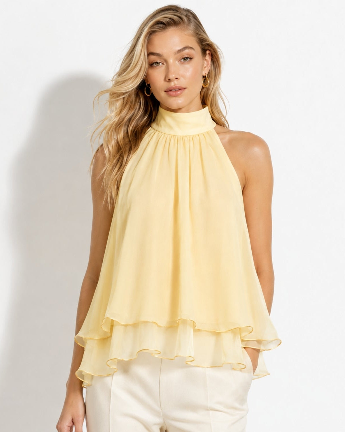 Front view of a blonde model wearing a pastel apricot chiffon tiered halter blouse with high neck and flowing ruffled layers