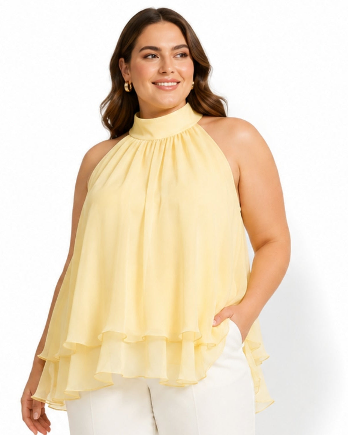 A woman modeling a pale yellow high-neck halter top with a layered ruffle hem, paired with white pants, against a plain white studio background.