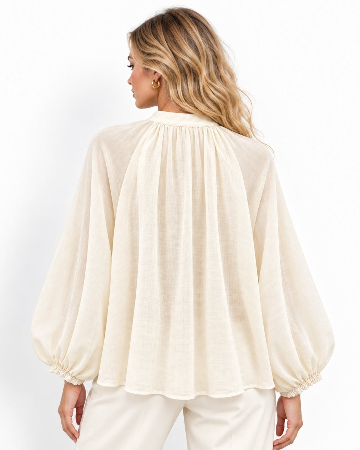 A woman shown from the back wearing a cream-colored long-sleeve blouse with a gathered, balloon-like silhouette and matching cream pants, set against a plain white studio background.