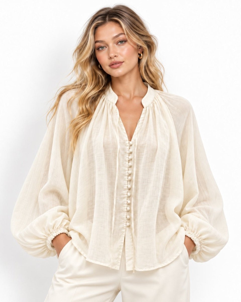 A woman modeling a cream-colored, lightweight long-sleeve blouse with a gathered high neck, button-down front, and voluminous balloon sleeves, paired with matching cream pants against a plain white background.