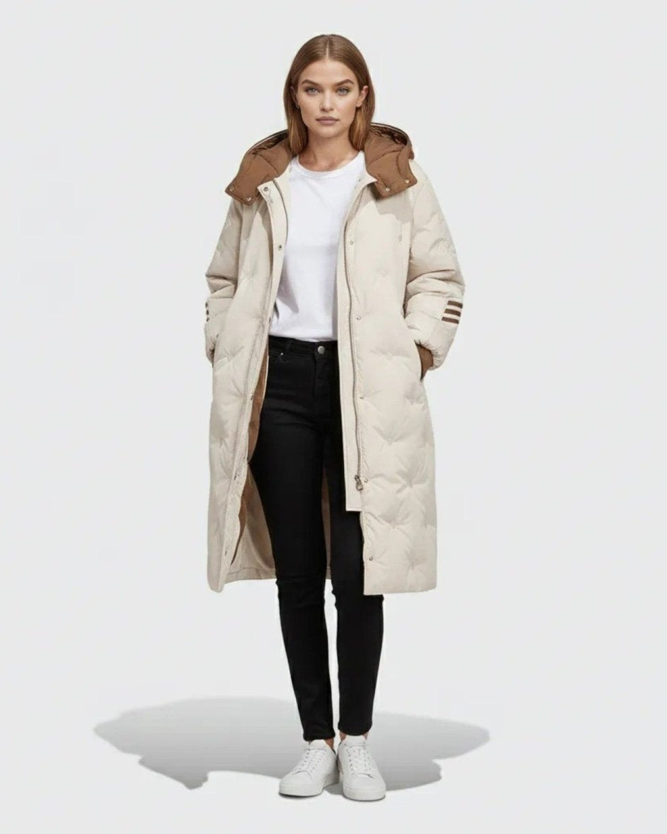 Model wearing the Arianne long quilted down puffer coat in ivory with a contrasting brown hood, styled with black jeans and white sneakers.
