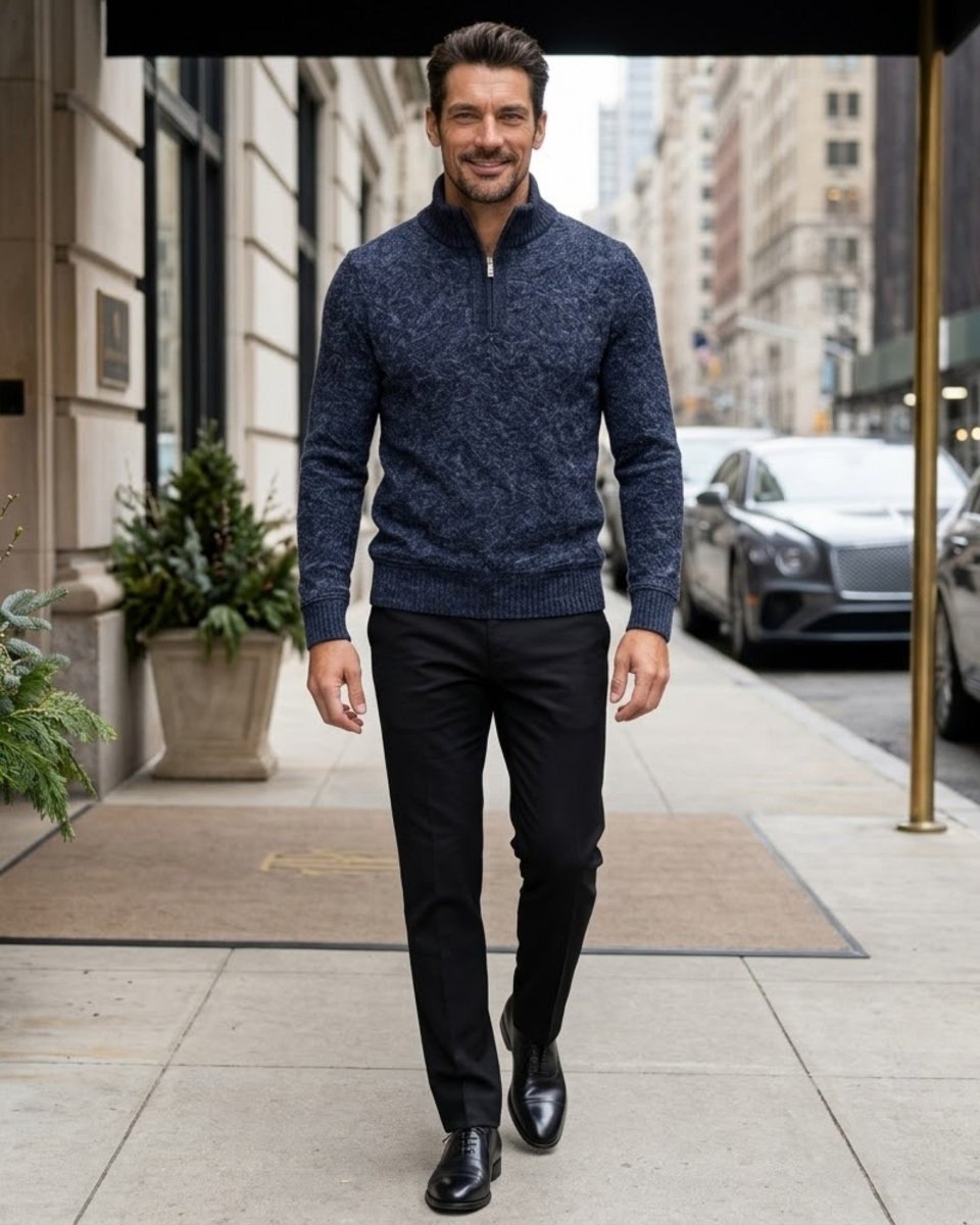 A man walking on a city sidewalk wearing a navy blue textured knit quarter-zip sweater, black trousers, and black dress shoes.
