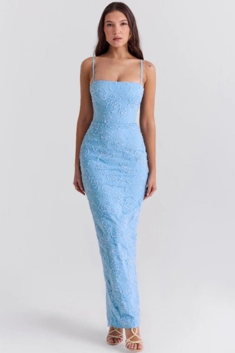 A woman modeling a light blue lace spaghetti-strap maxi dress against a plain light gray studio background.