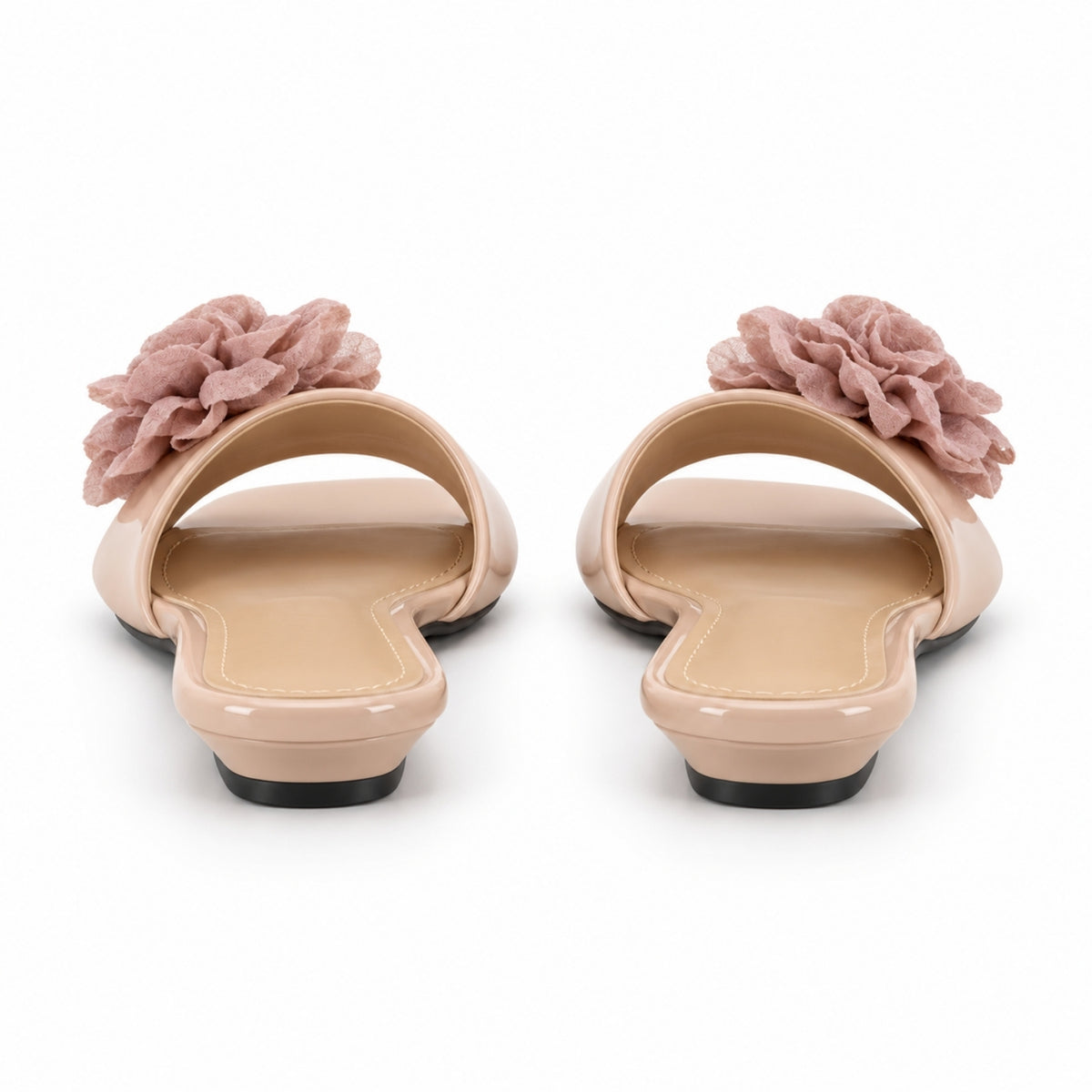 A pair of women's open-toe slide sandals in a glossy nude beige finish, featuring a large dusty rose fabric flower applique on the outer side of each shoe, shown from a rear three-quarter view on a white background.