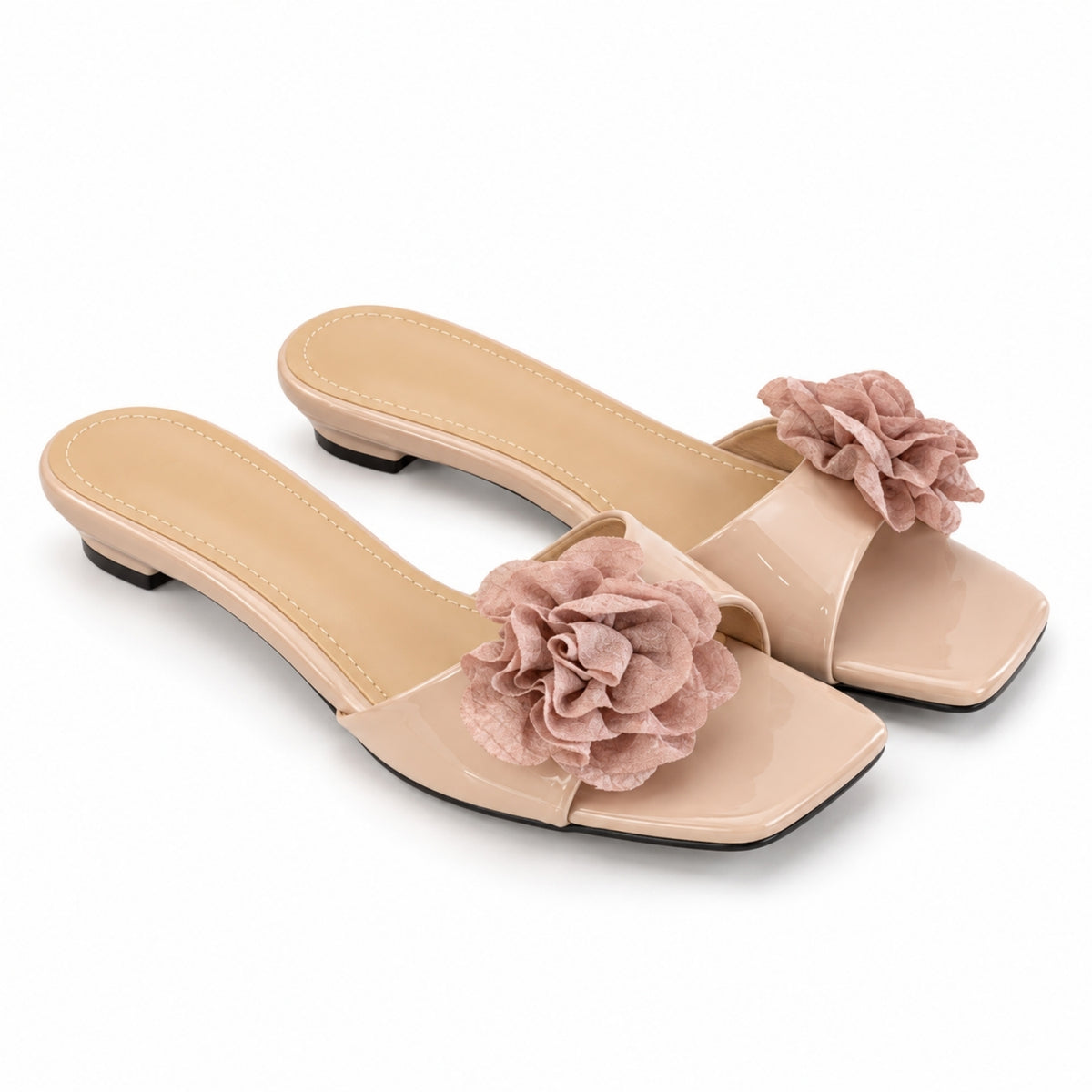 A pair of nude patent leather mule sandals with a large dusty pink fabric flower embellishment on the toe strap, set against a plain white background.