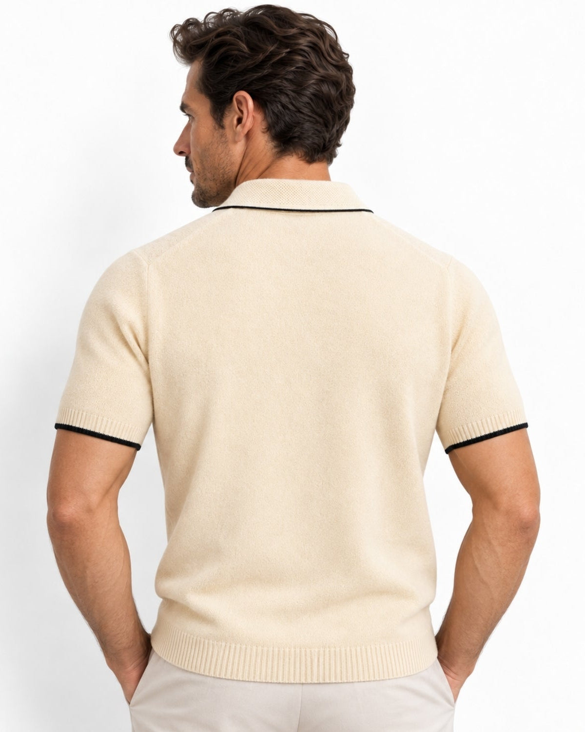 A man shown from the back wearing a beige-colored short-sleeve knit polo shirt with black piping on the collar and sleeve cuffs, paired with light beige trousers, against a plain white studio background.