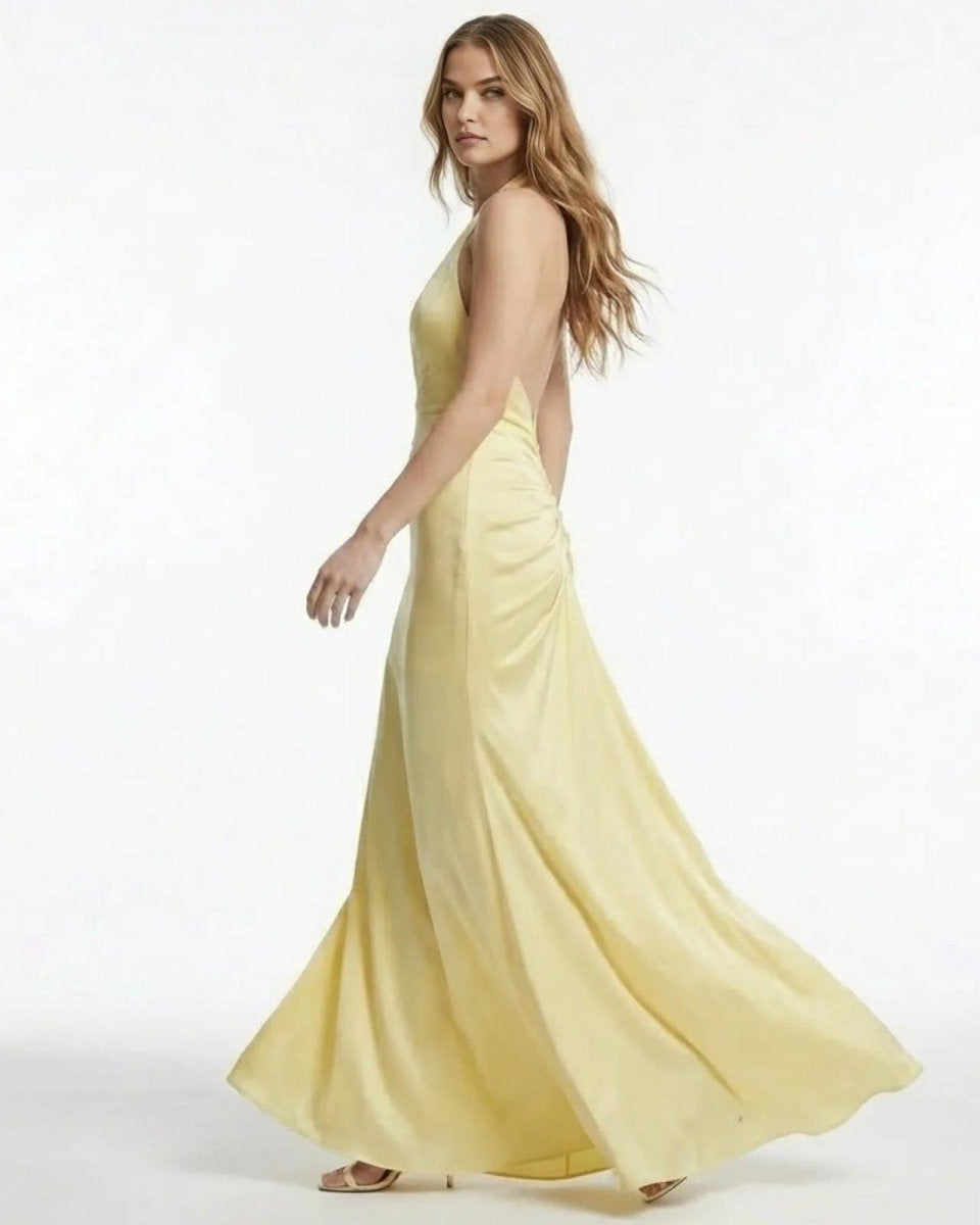 Side view of a model in the Beverly light yellow backless maxi dress, showing the open back design and flowing mermaid skirt.
