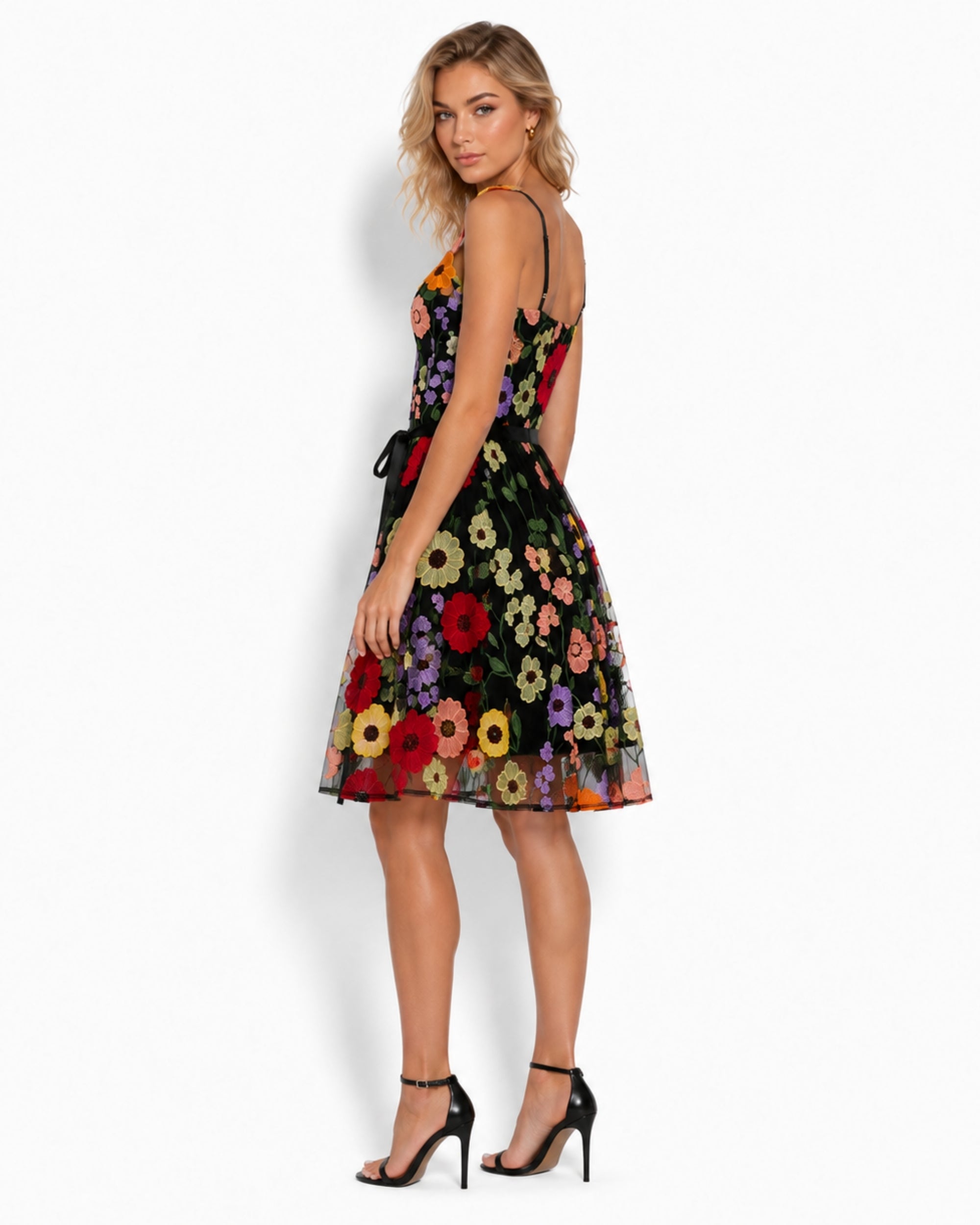 A woman modeling a sleeveless black midi dress with a vibrant multicolor floral print, shown from a three-quarters back angle against a plain white studio background.