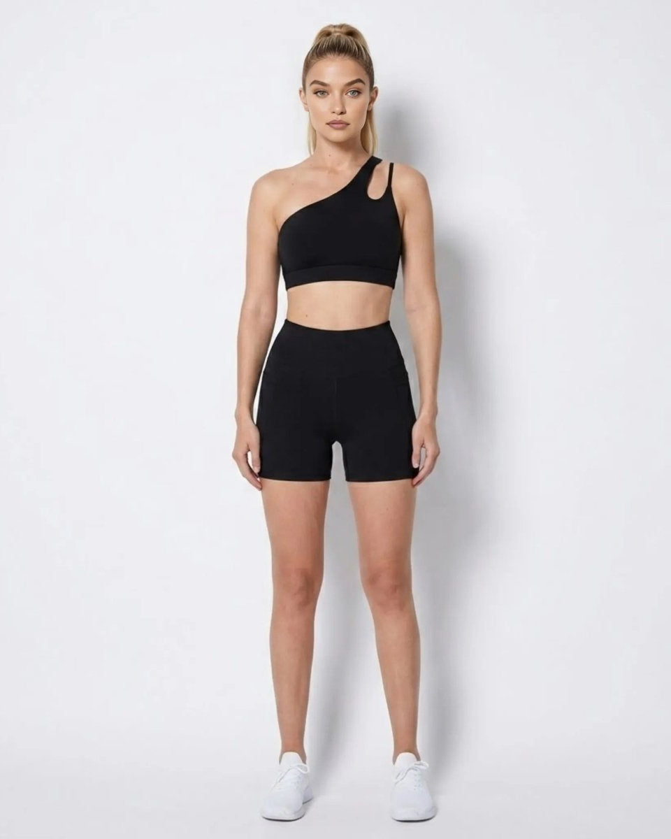 Woman wearing black asymmetrical one shoulder activewear set with high waisted biker shorts facing forward