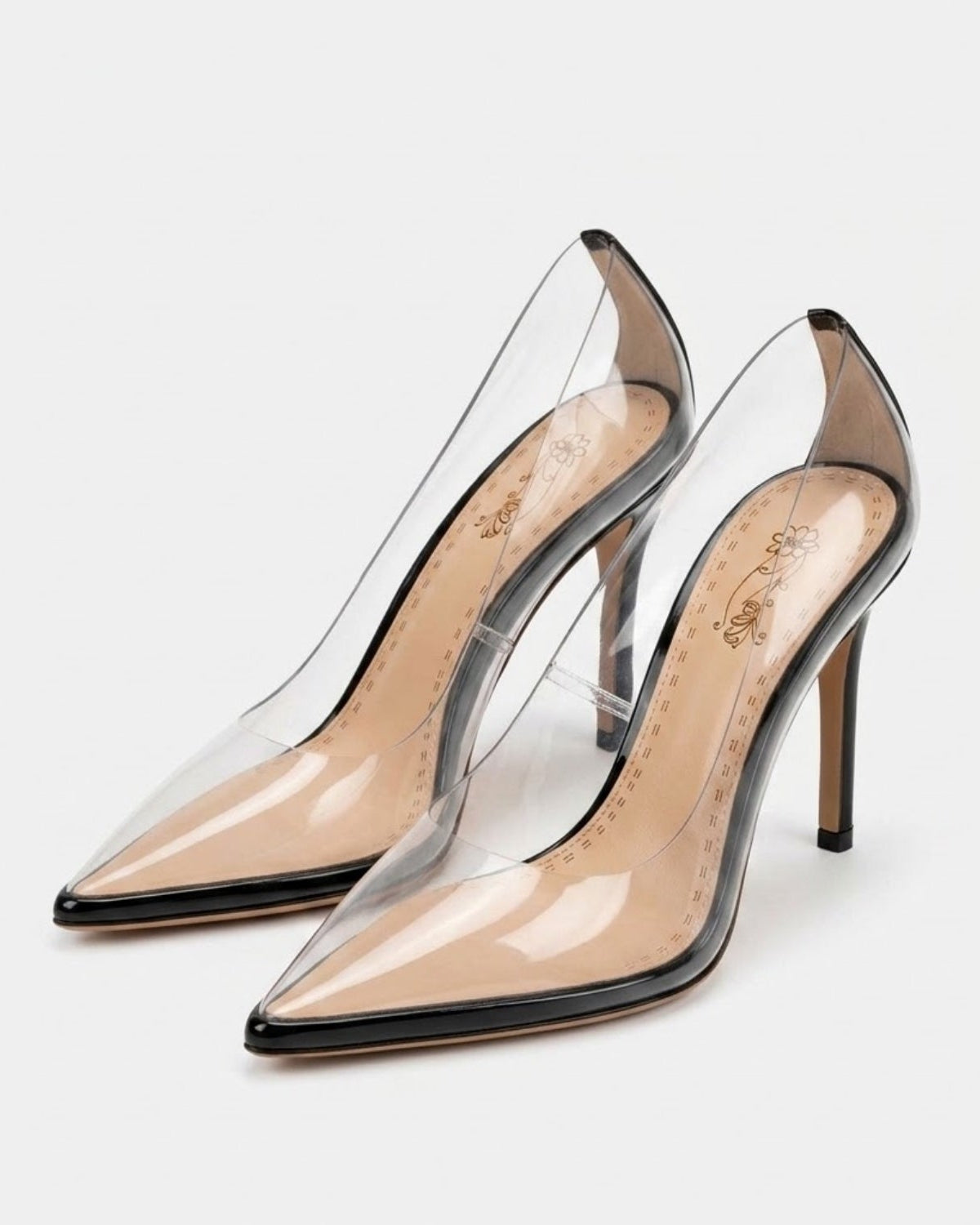 A pair of clear patent leather pointed-toe pumps with slim stiletto heels, shown on a light gray background.