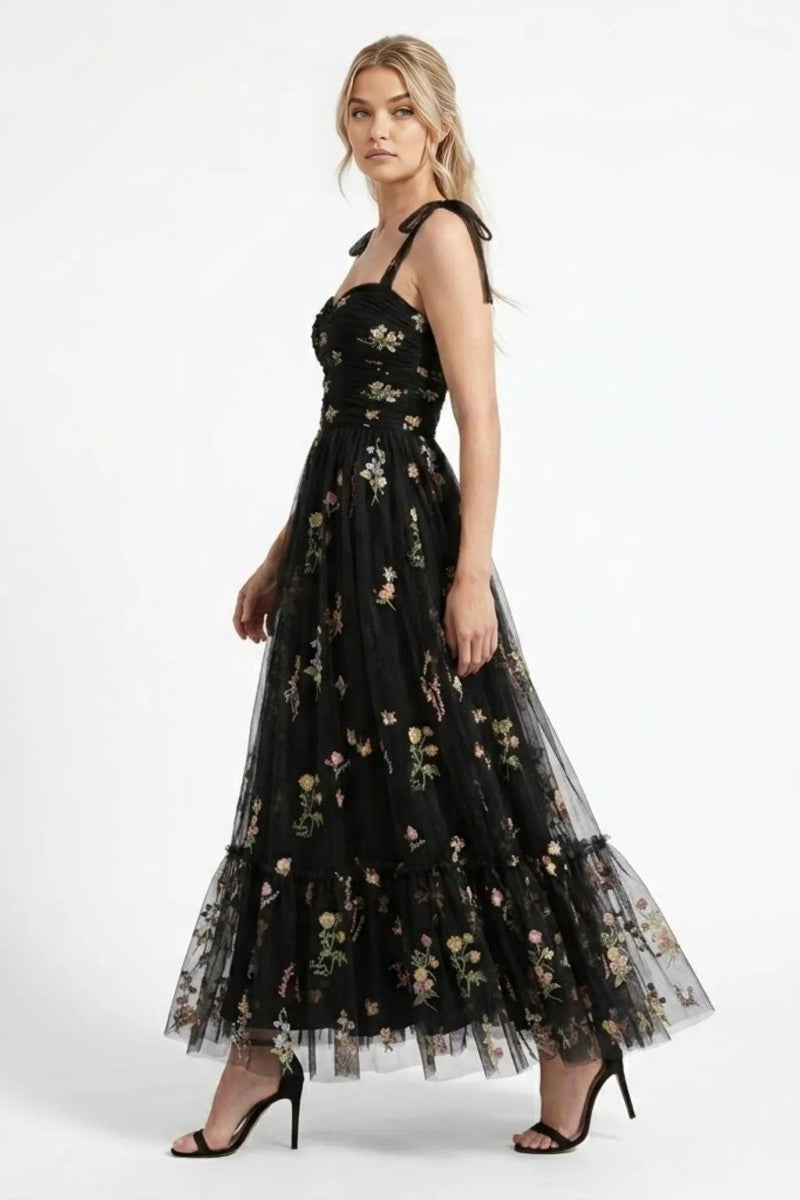 Side profile of woman walking in Fenlo Form black floral embroidered tulle maxi gown showing tiered skirt and botanical details.