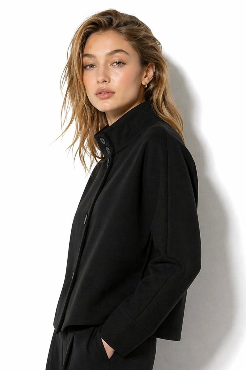 Side profile of the minimalist black mock neck boxy jacket by Fenlo Form styled with matching black trousers.