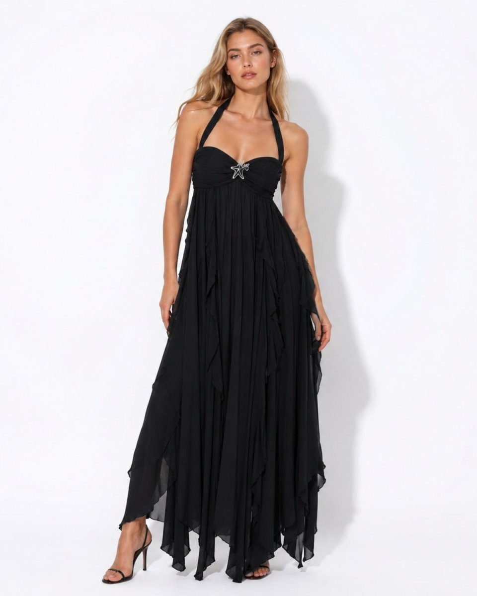 A woman modeling a black halter-neck maxi dress with a sweetheart neckline, ruched bodice, and layered ruffle skirt, paired with black high heels against a white studio background.