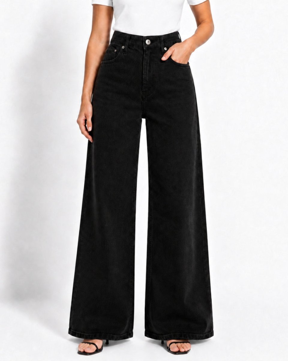 A model wearing black wide-leg denim jeans with a white t-shirt and black sandals, standing against a light gray studio background.