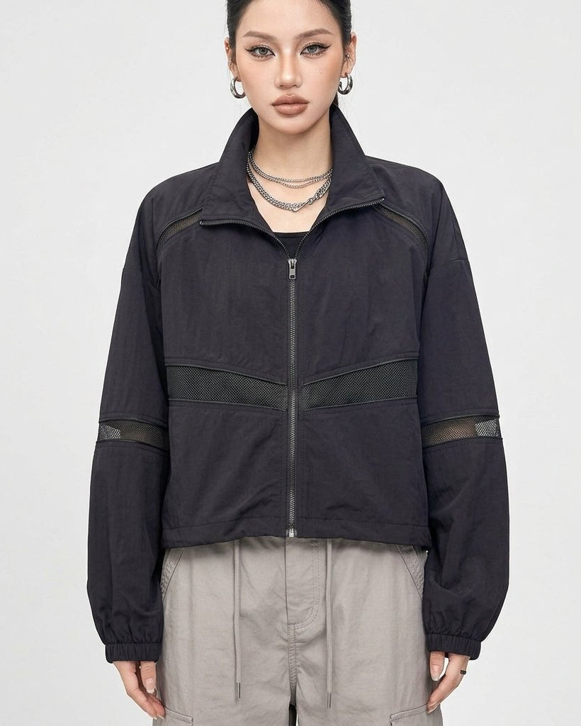 Front view of Kouvr women's black cropped windbreaker jacket with sheer mesh panels and full zip closure on studio model