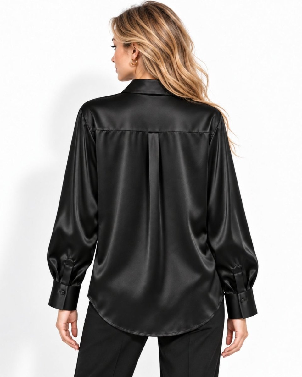 A woman shown from the back wearing a black silk long-sleeve button-up shirt and black pants, photographed against a clean white studio background.