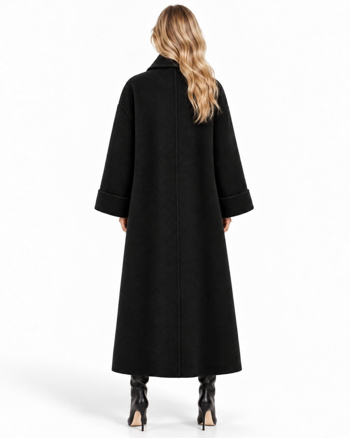 A woman viewed from the back wearing a long black coat with wide sleeves and black pointed-toe heels against a plain white studio background.
