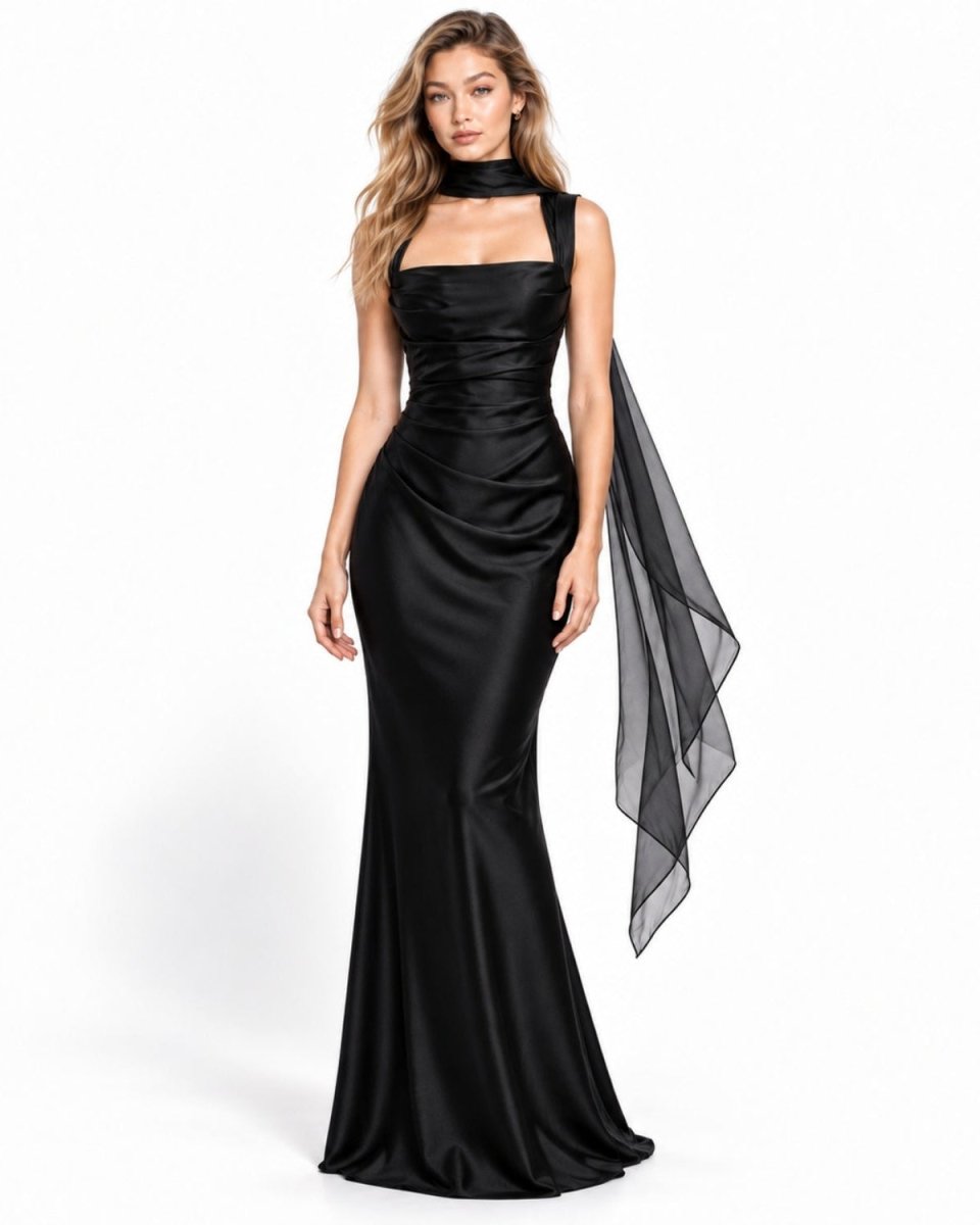 A woman modeling a floor-length black satin gown with a high choker neckline, square neckline, ruched bodice, and a sheer black draped overlay on one side, photographed against a clean white studio background.