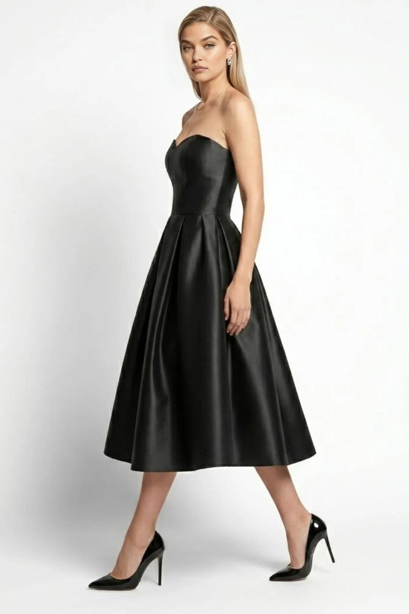 Side profile of model walking in black satin a-line midi dress with strapless sweetheart bodice by Fenlo Form