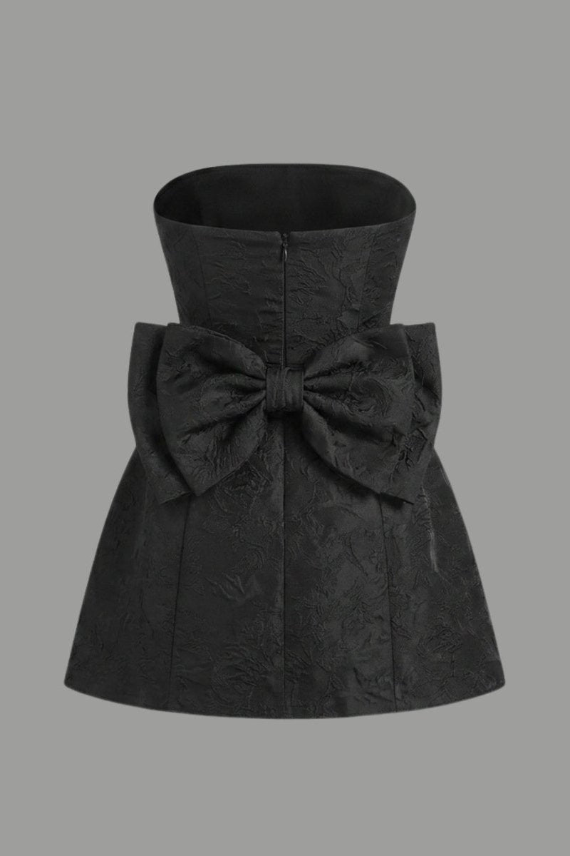 Ghost mannequin back styling of a black mini dress highlighting the oversized attached statement bow and hidden zipper.