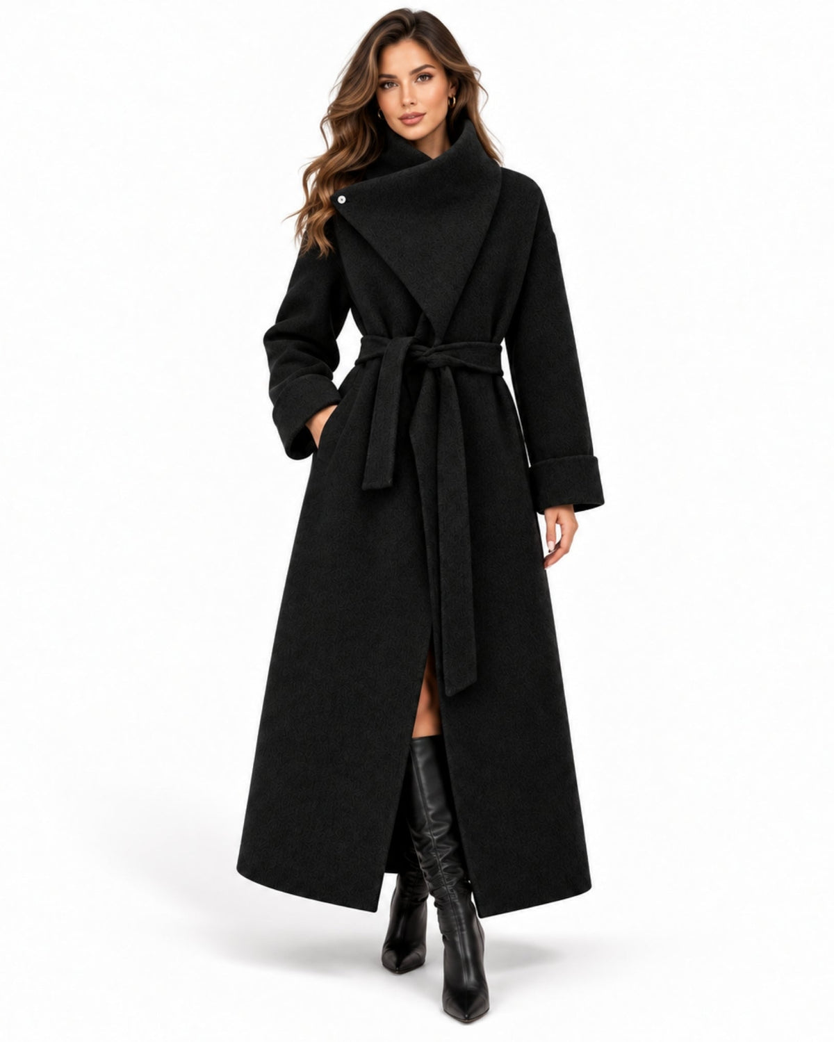A woman modeling a long black wrap coat with a high collar, belted waist, and front slit, paired with black knee-high boots on a plain white studio background.