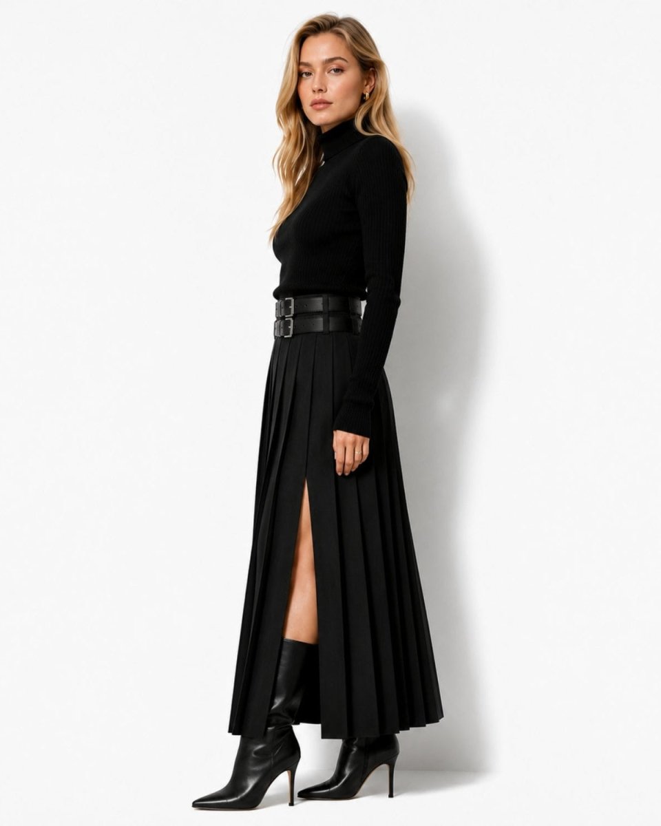 A woman modeling a black long-sleeve mock-neck top paired with a black pleated midi skirt featuring a front slit and a wide black belt, styled with black heeled ankle boots against a plain white studio background.