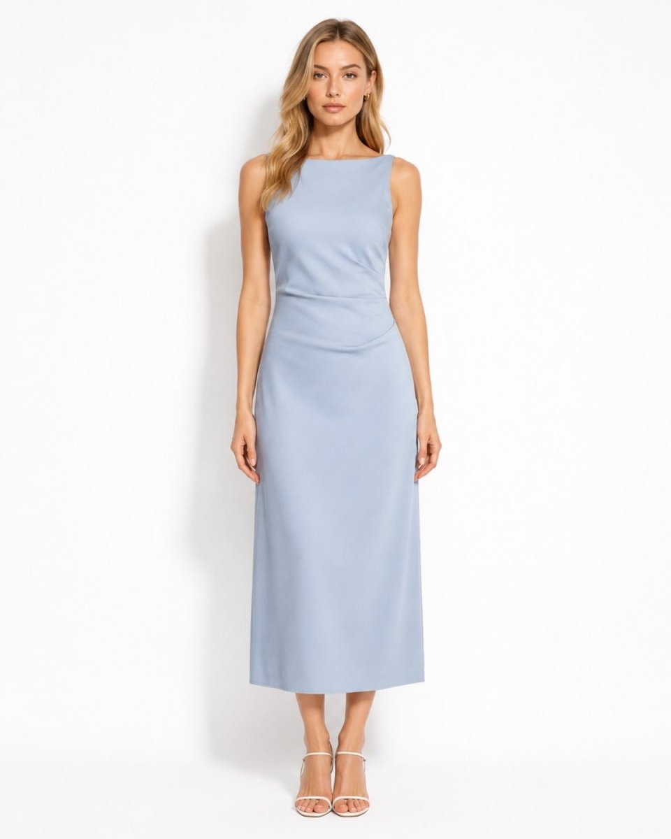 A woman modeling a sleeveless light blue midi dress with a boat neckline and a draped waist detail, paired with clear high-heeled sandals, against a plain white studio background.
