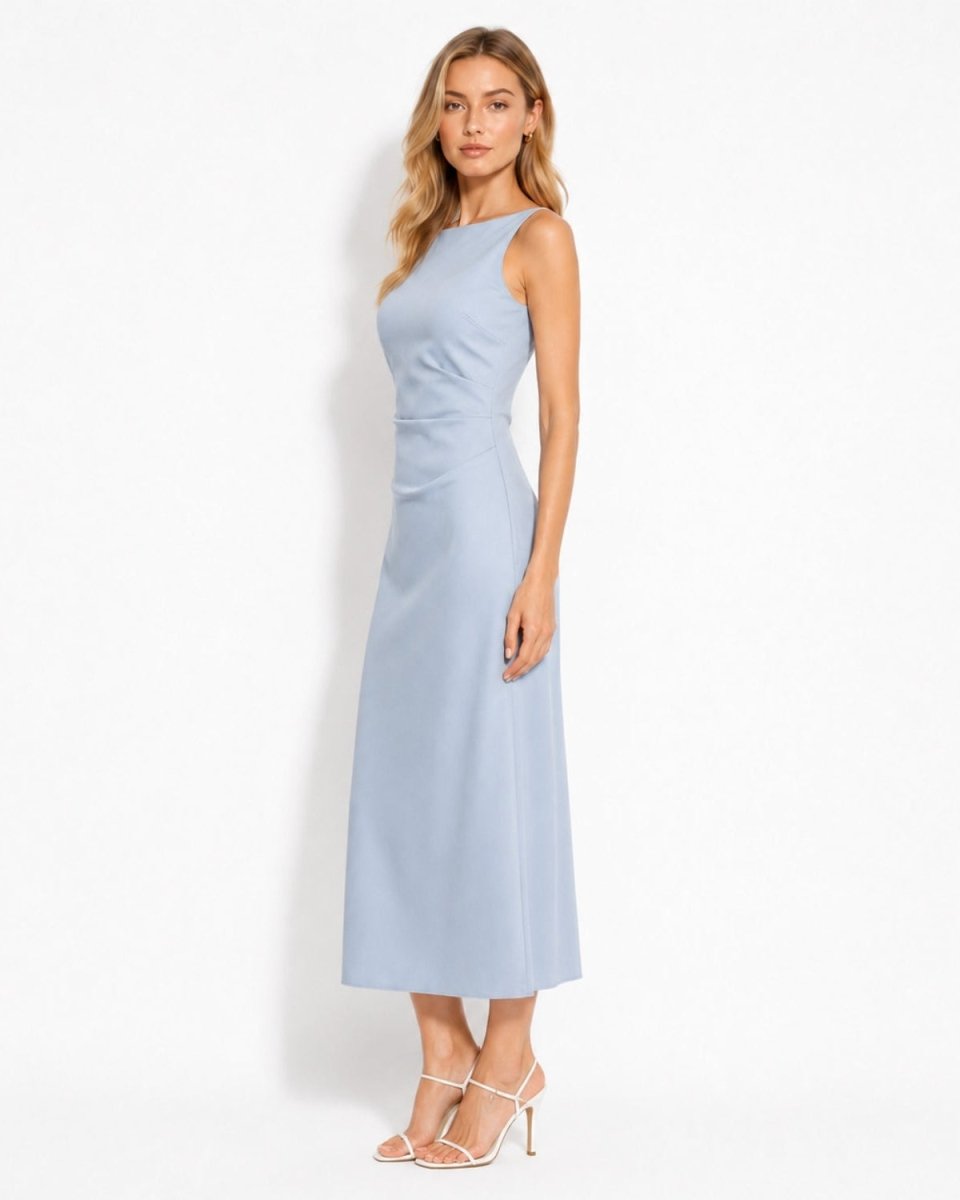 A woman modeling a sleeveless light blue midi dress with a high neckline and gathered waist, paired with white strappy high-heeled sandals, against a plain white studio background.