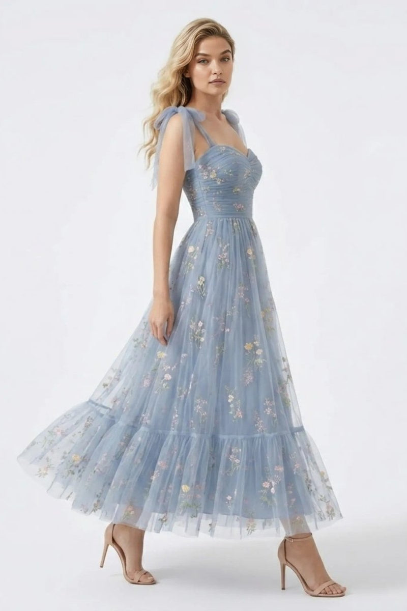 Side angle of a blonde model twirling in the Fenlo Form blue tulle tiered maxi dress showcasing vibrant floral embroidery and flowy A-line skirt.
