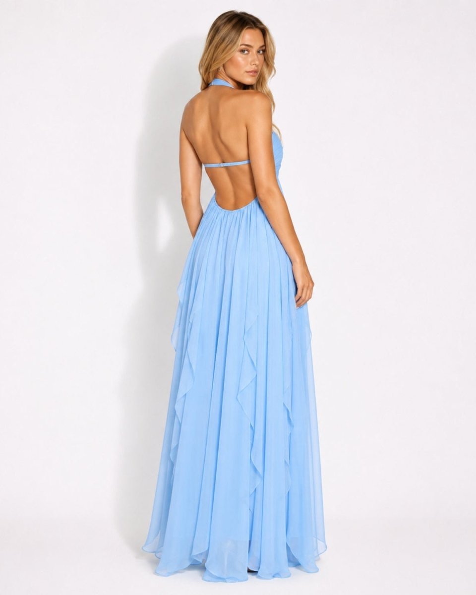 A woman modeling a light blue halter-neck maxi dress from the back, showing an open back and ruffled skirt details, set against a plain white studio background.