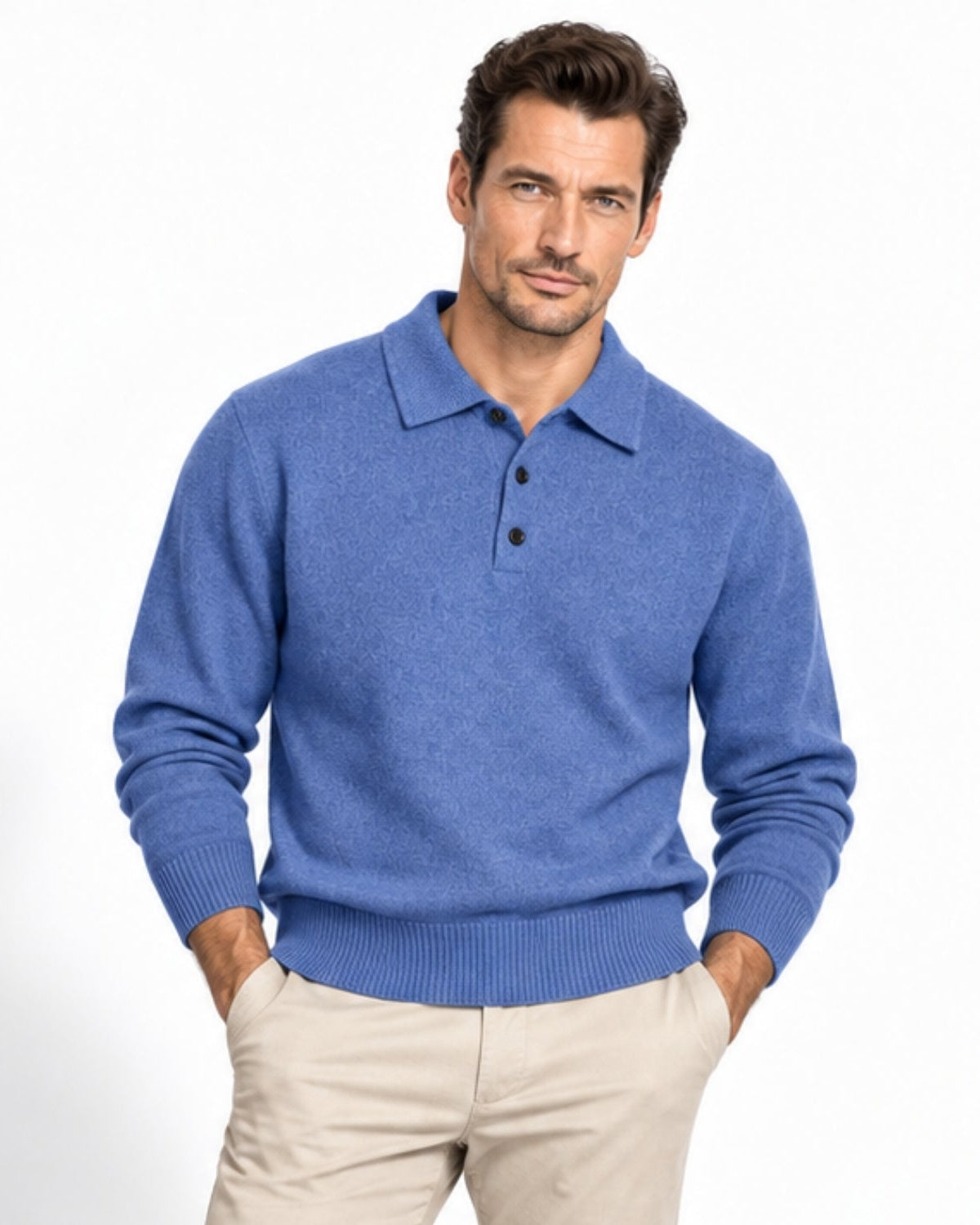 A man wearing a blue knit polo sweater and beige trousers, standing against a clean white studio background.