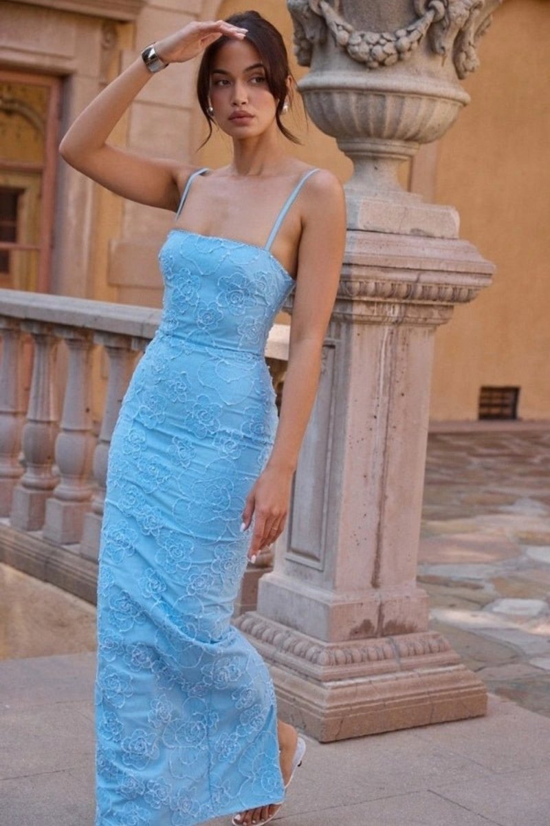 Woman in a blue lace dress standing outdoors near classical architecture.