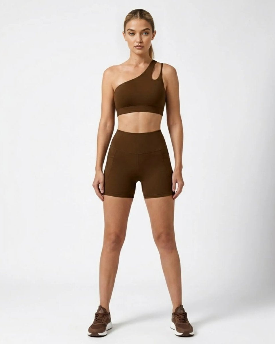 Woman wearing dark brown one shoulder sports bra and high waisted biker shorts activewear set front view