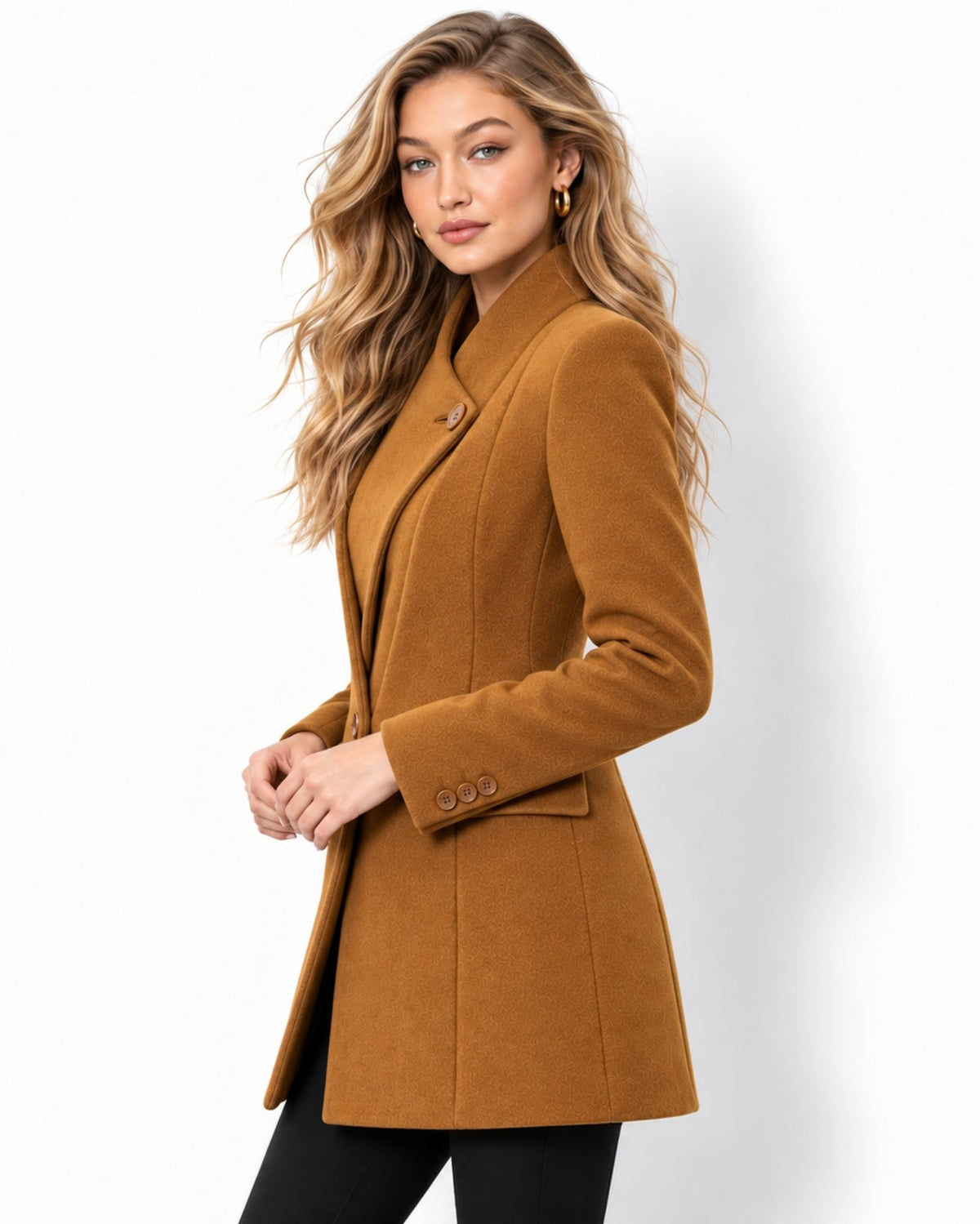 A woman modeling a camel brown double-breasted coat with a peak lapel and three-button closure on the sleeve, paired with black pants against a white studio background.