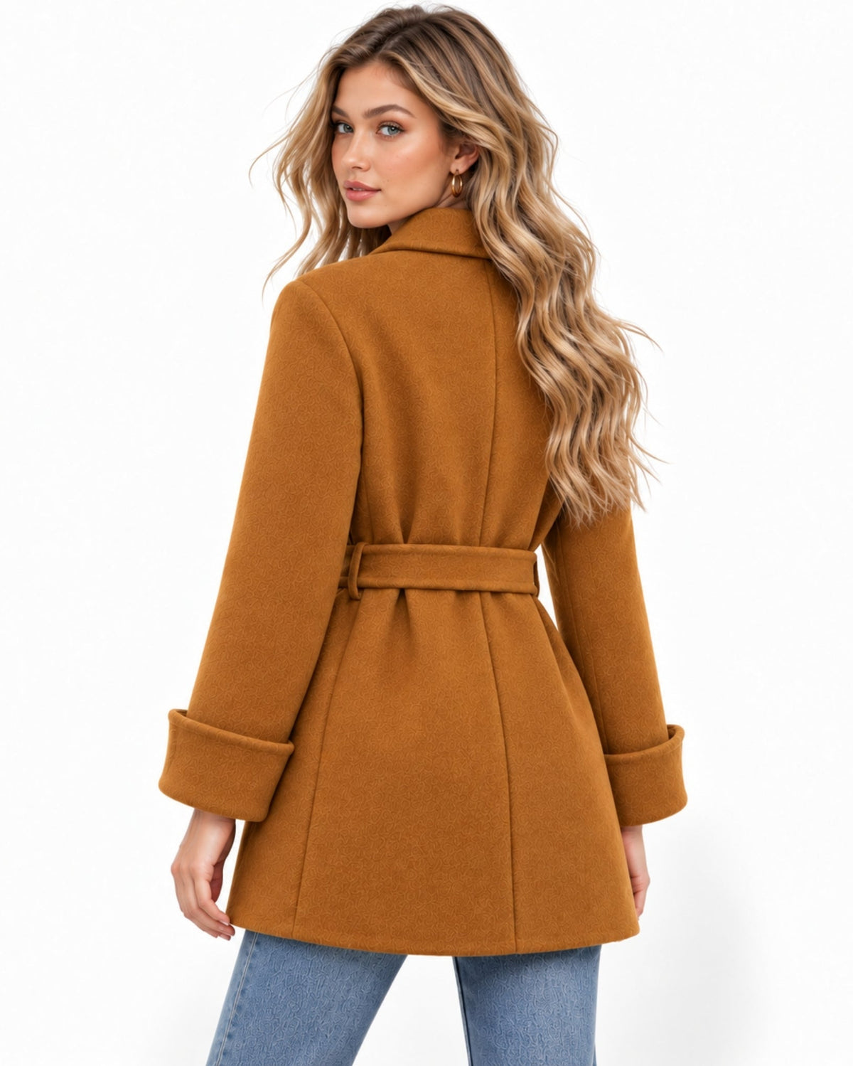 A woman modeling a camel brown belted coat from the back, paired with blue jeans, against a plain white background.
