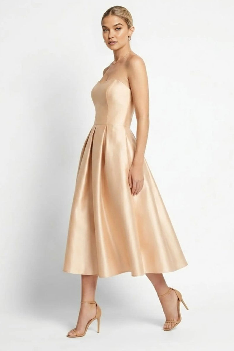 Side view of elegant champagne satin A-line cocktail dress with pleated midi skirt and strappy heels