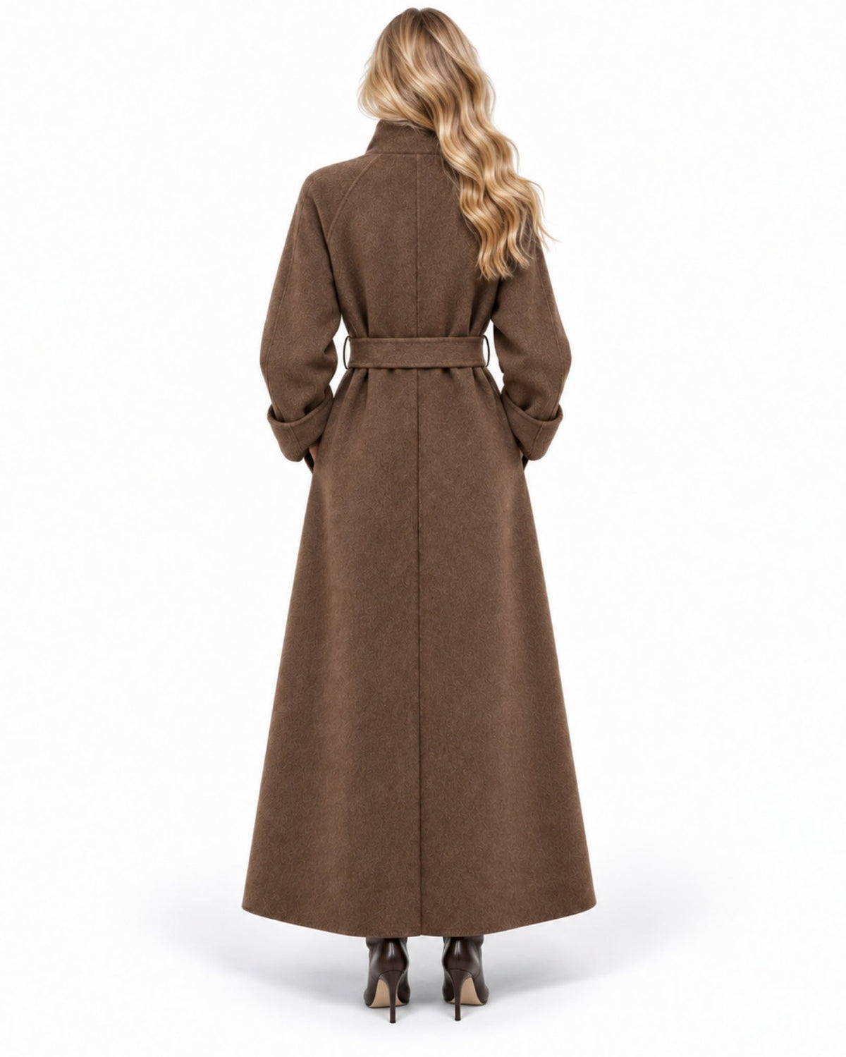 A woman viewed from the back wearing a long brown belted coat with long sleeves and a high collar, paired with dark pointed-toe heels, against a plain white studio background.