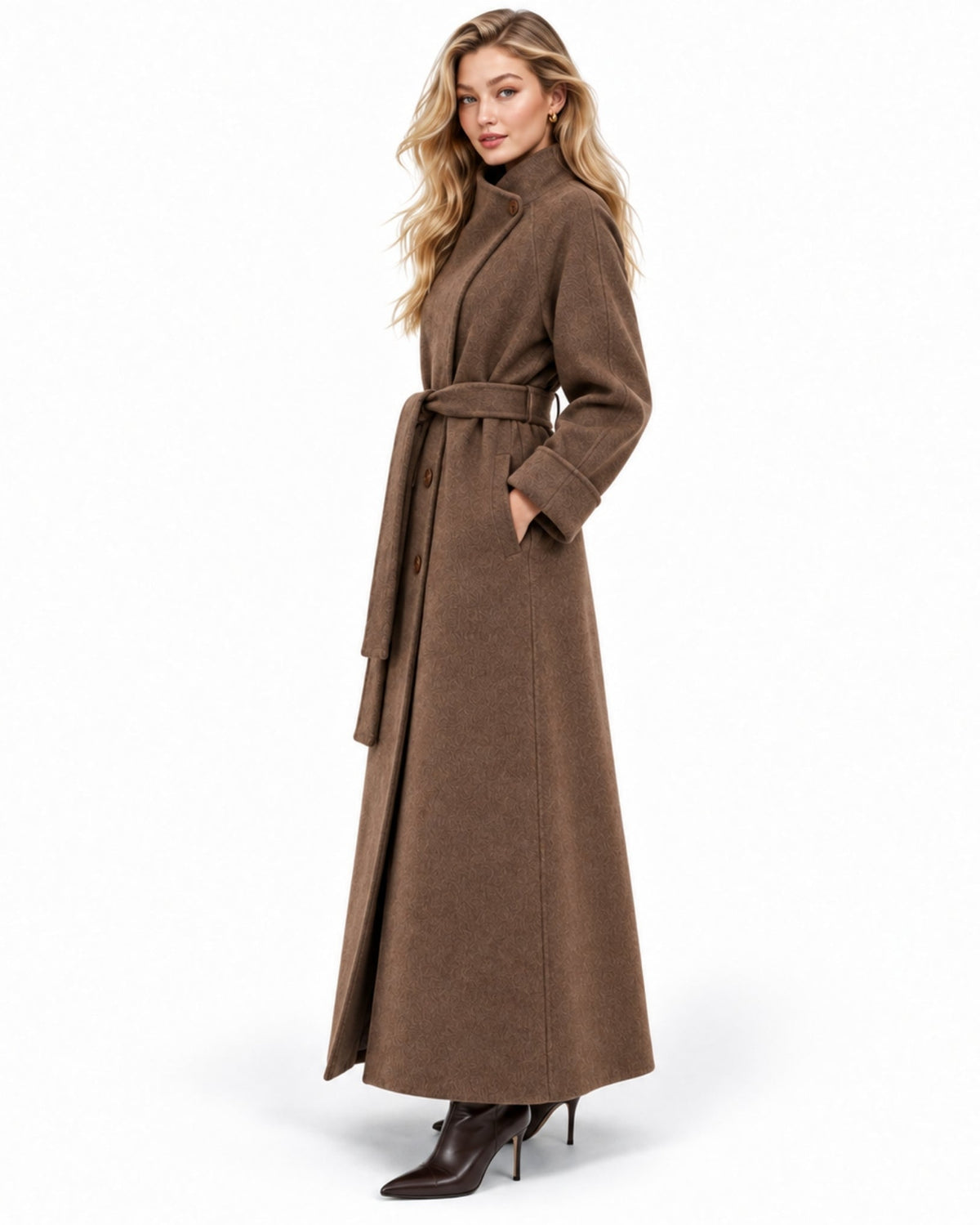 A woman modeling a long brown belted coat with a high mock neck, paired with dark brown pointed-toe ankle boots, against a plain white studio background.