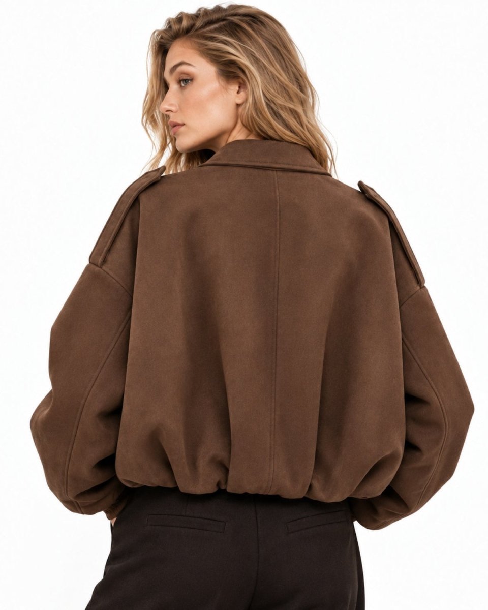 A woman shown from the back wearing a cropped brown suede-like jacket with voluminous sleeves and dark pants, photographed against a plain white studio background.