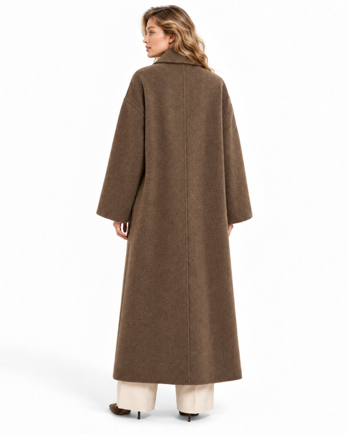 A woman shown from the back wearing a long, wide-sleeved brown coat over cream wide-leg pants, photographed against a clean white studio background.
